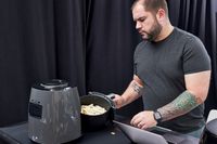 A person placing a basket of fries into a Ninja air fryer.