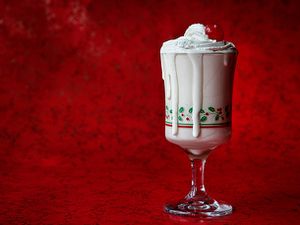 A DIY McDonald's egg nog milkshake, topped with whipped cream and a maraschino cherry in a glass holiday cup, on a red background.