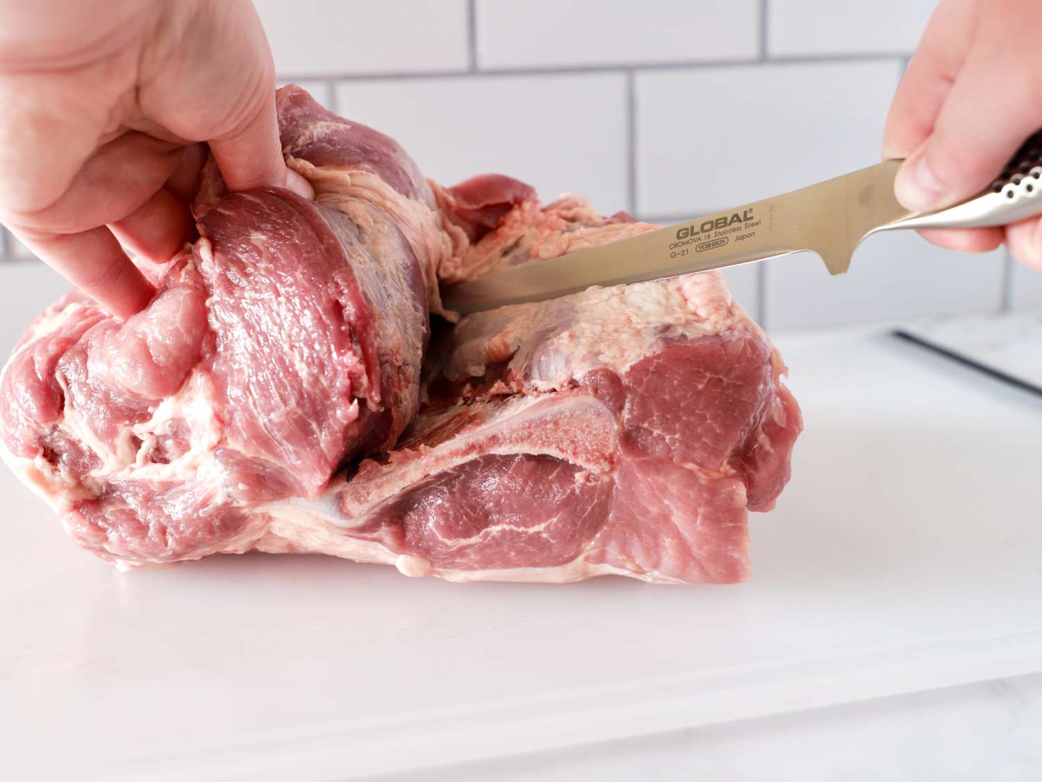 A person using the Global boning knife to cut meat.