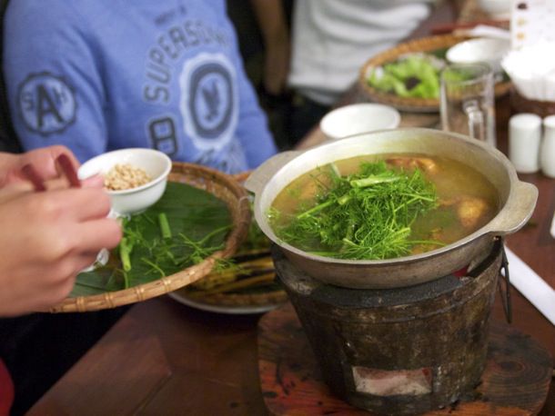 Greens being placed into a pot of Cha Ca Hanoi