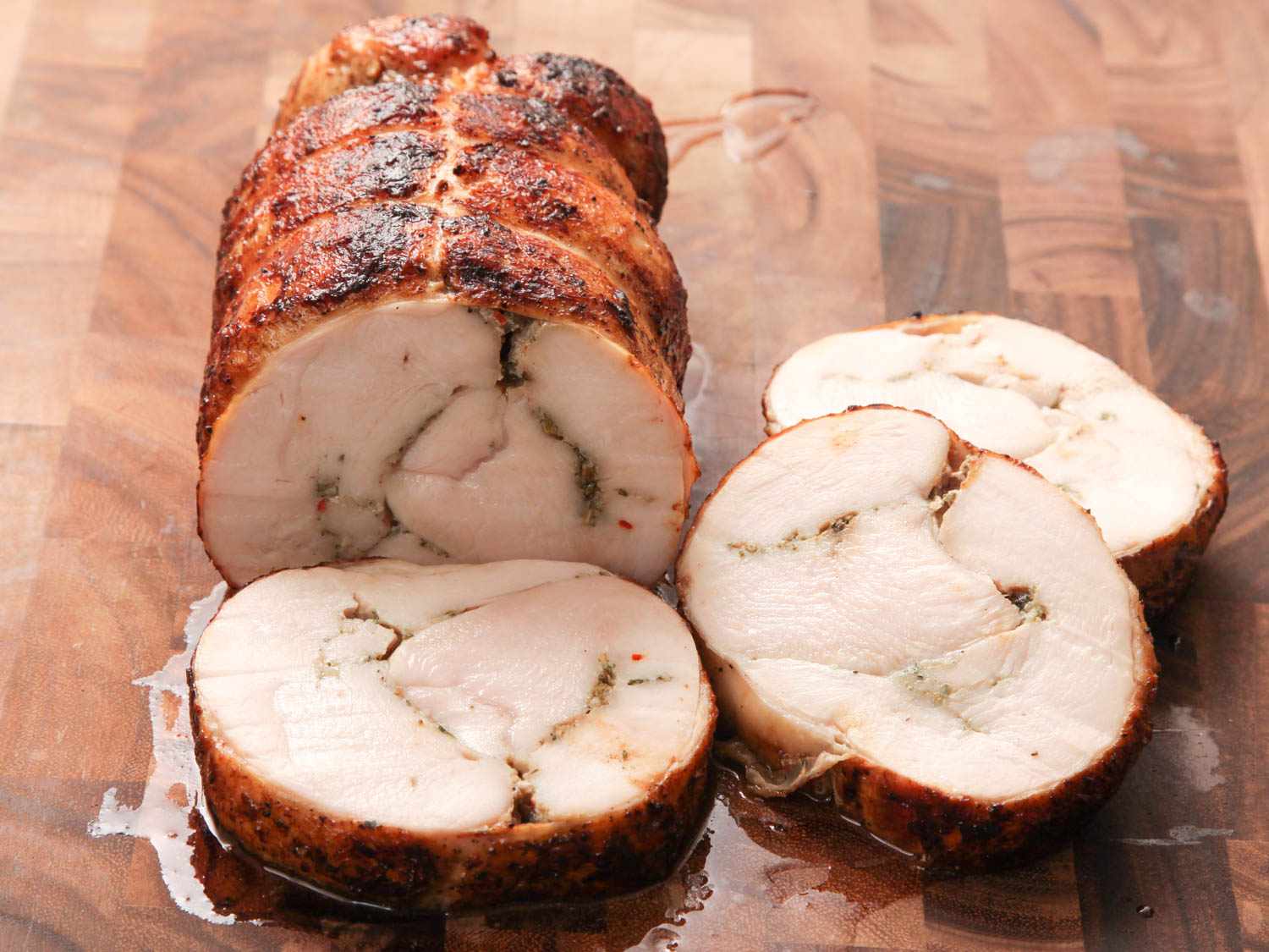 Closeup of a finished turkey porchetta partially sliced on a cutting board.