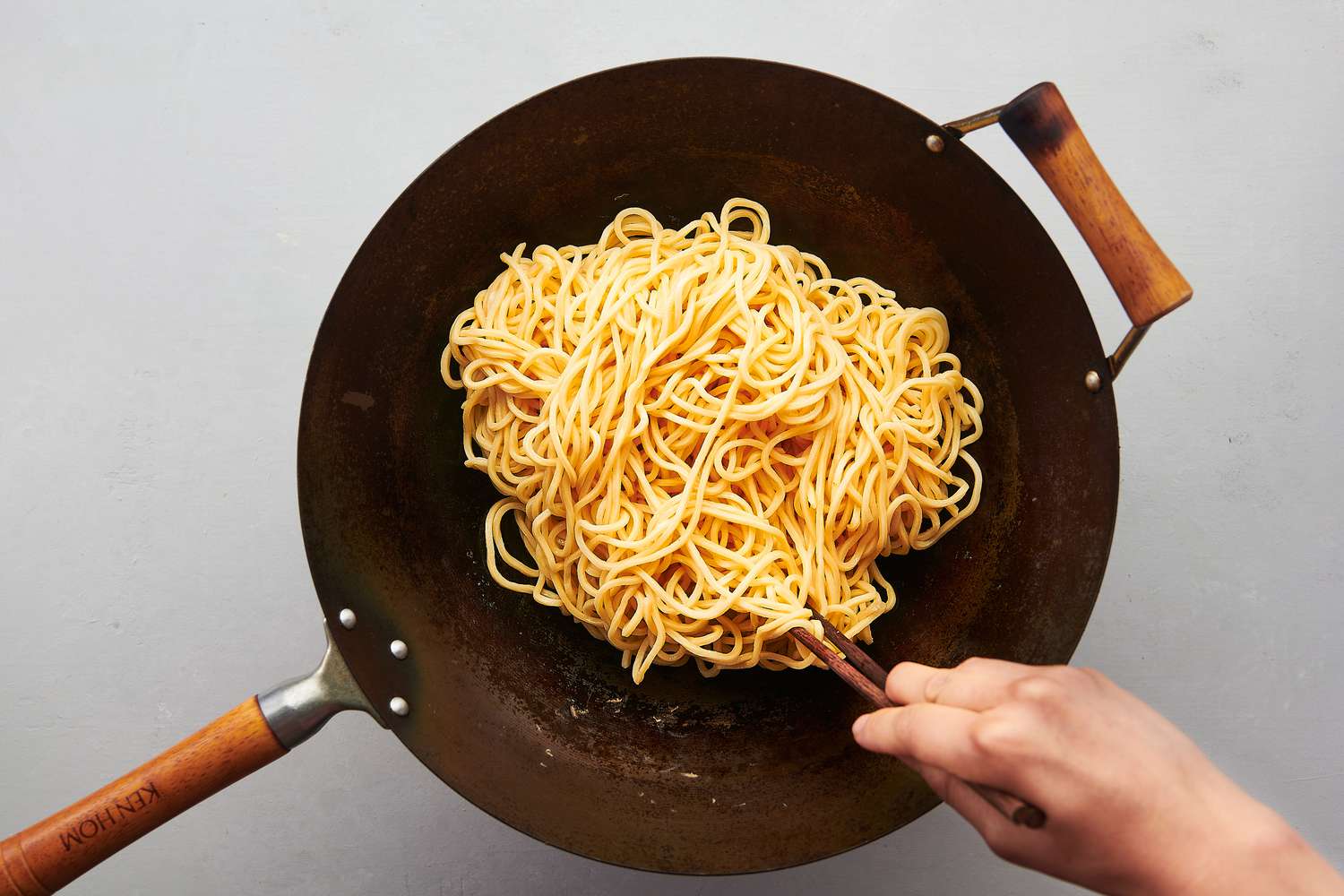 Noodles stirred inside wok over high heat