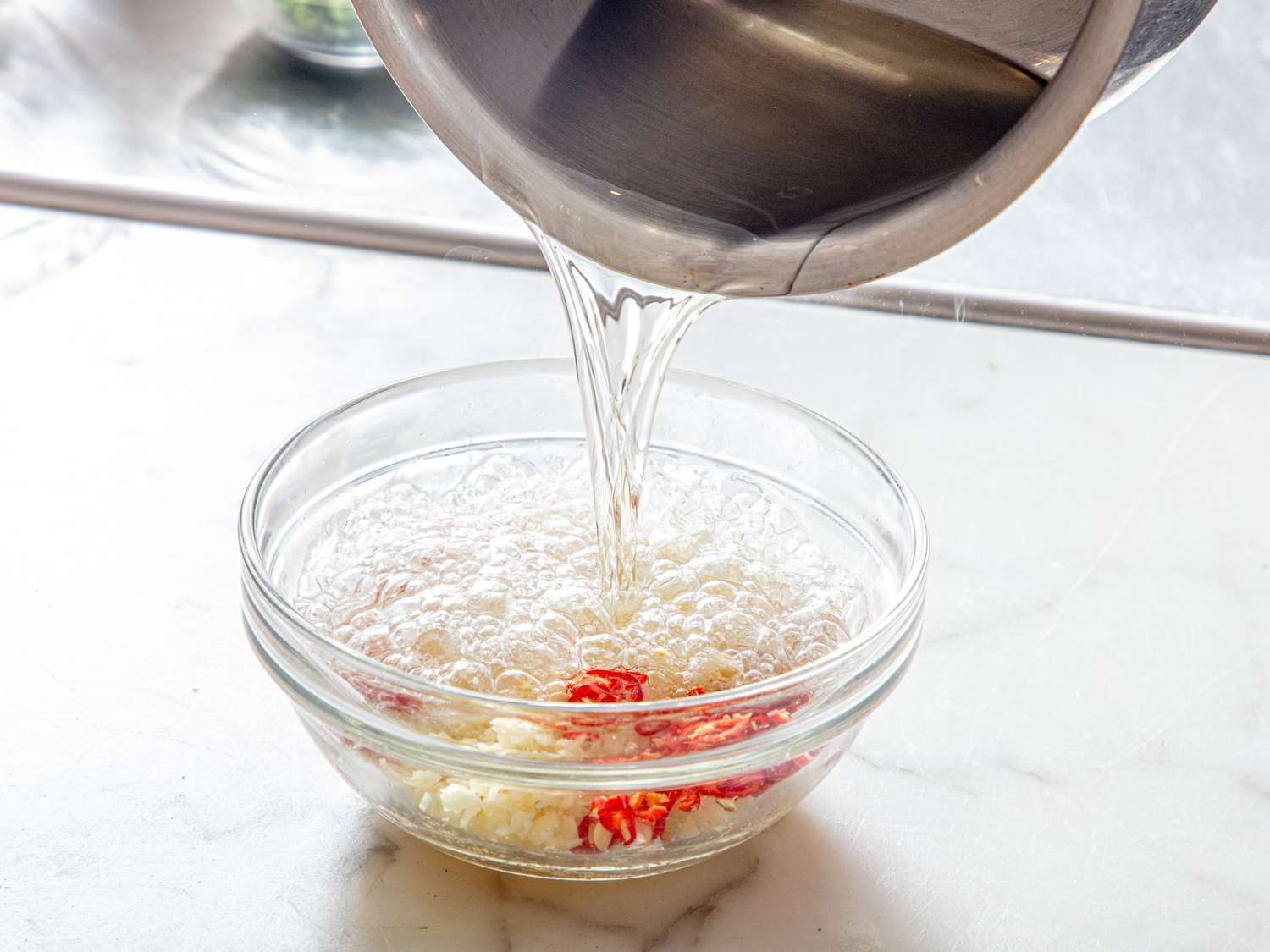 Hot liquid being poured into a bowl containing chili peppers and minced garlic