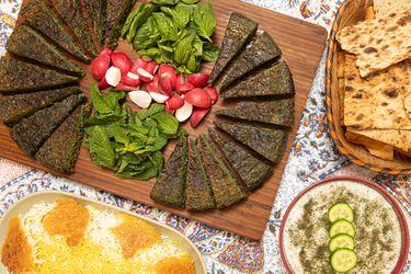 Platter of sliced kookoo, flatbread, and rice on a floral tablecloth
