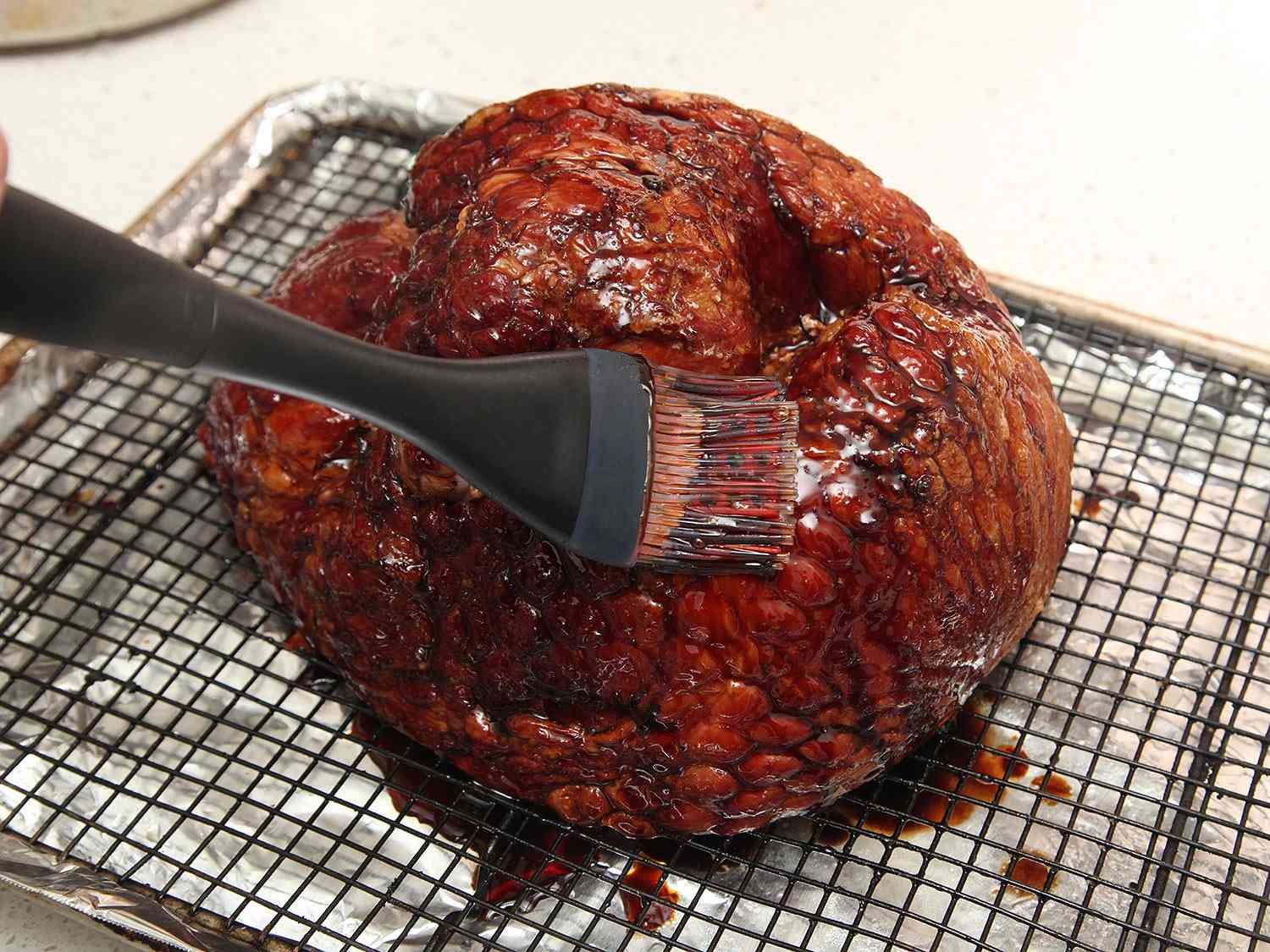 Brushing glaze onto a ham on a wire rack over a rimmed baking sheet. 