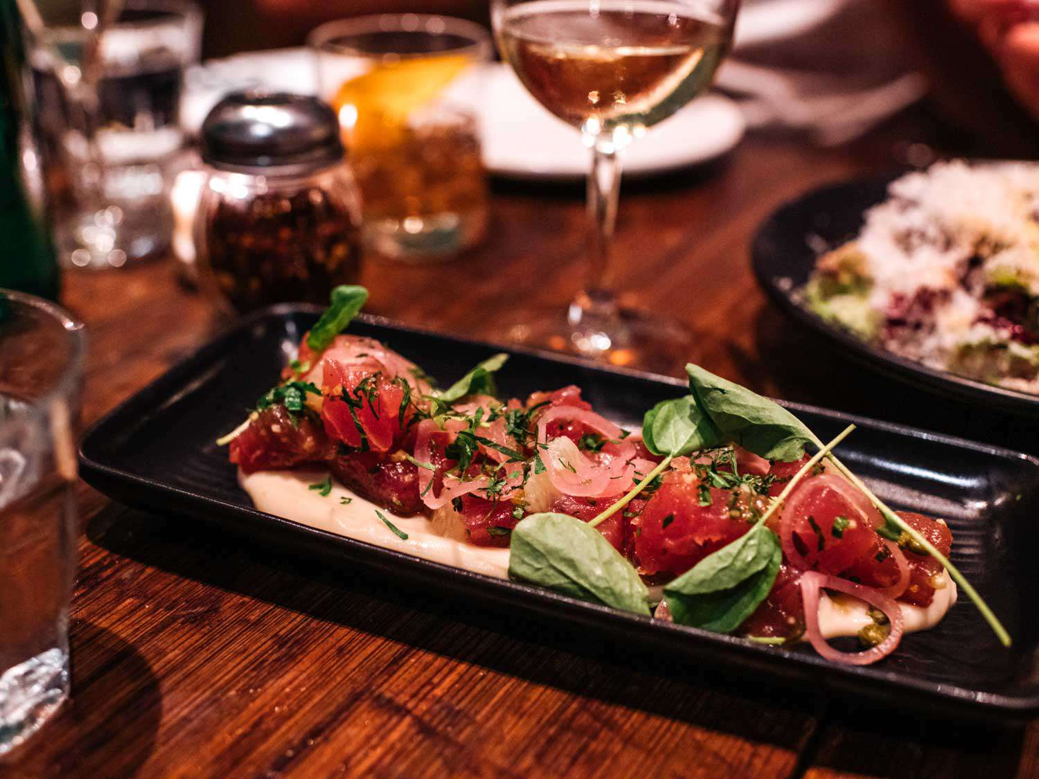 Tuna crudo at Paladar 511, in a black serving dish on a table with wine, drinking glasses, and condiments.