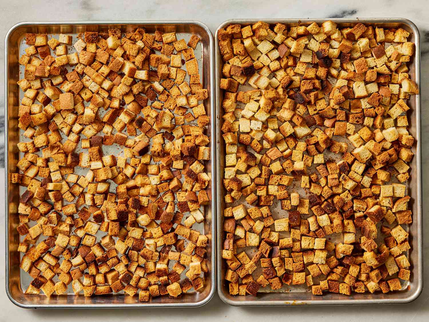 2 sheet pans side by side with baked bread cubes on them 