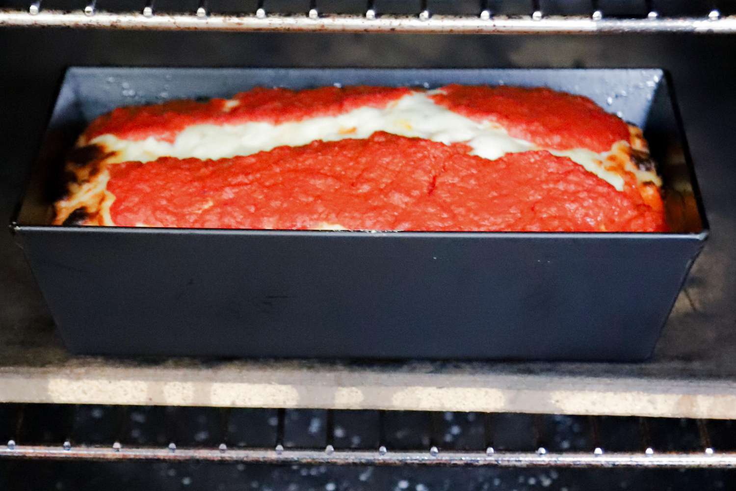 A dark metal deep-dish pizza pan in the oven