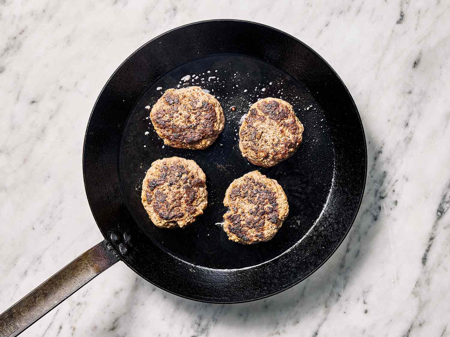 Four cooked patties in a black skillet on a marble surface