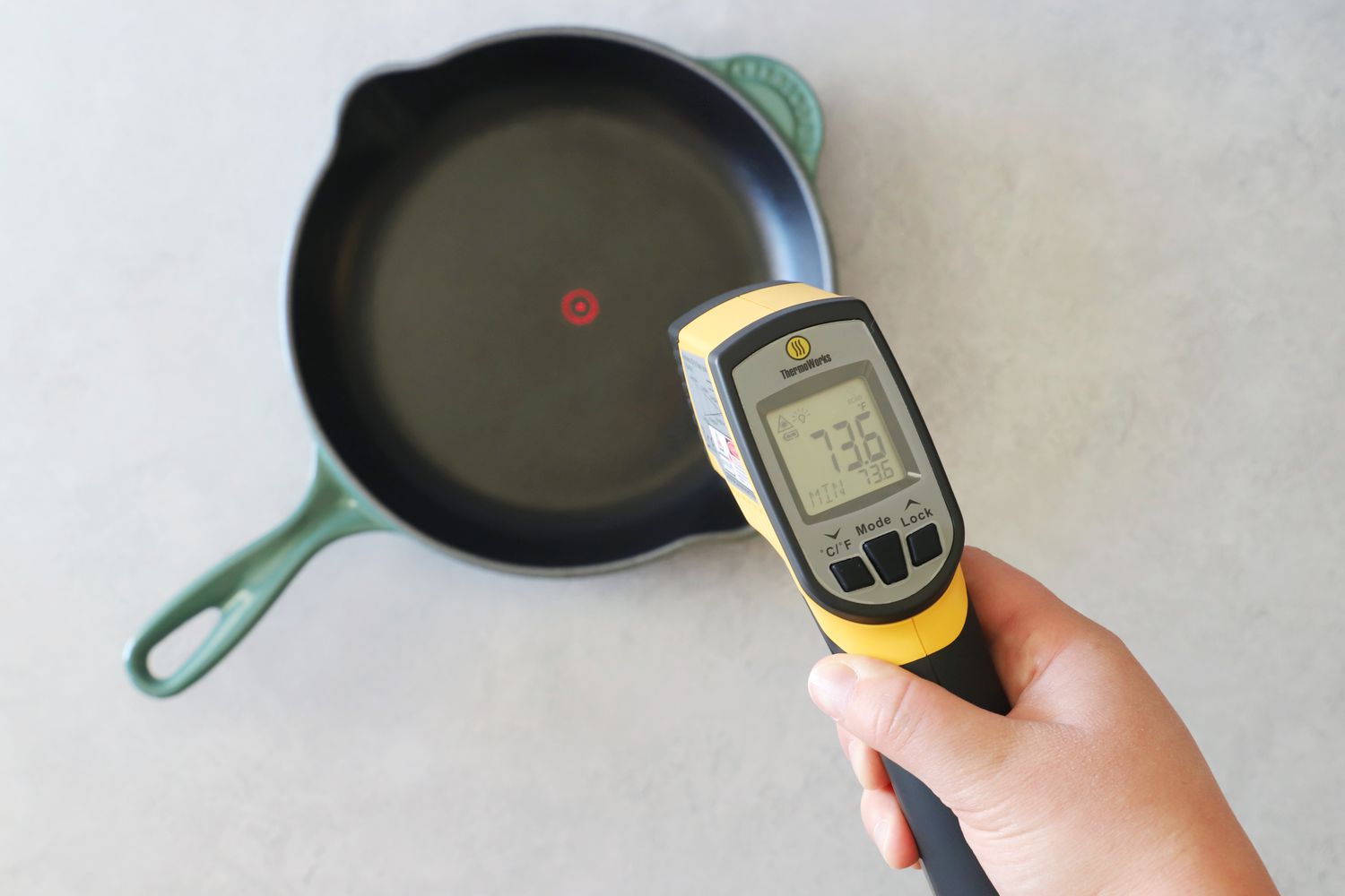 A person pointing an infrared thermometer at an enameled cast iron skillet.