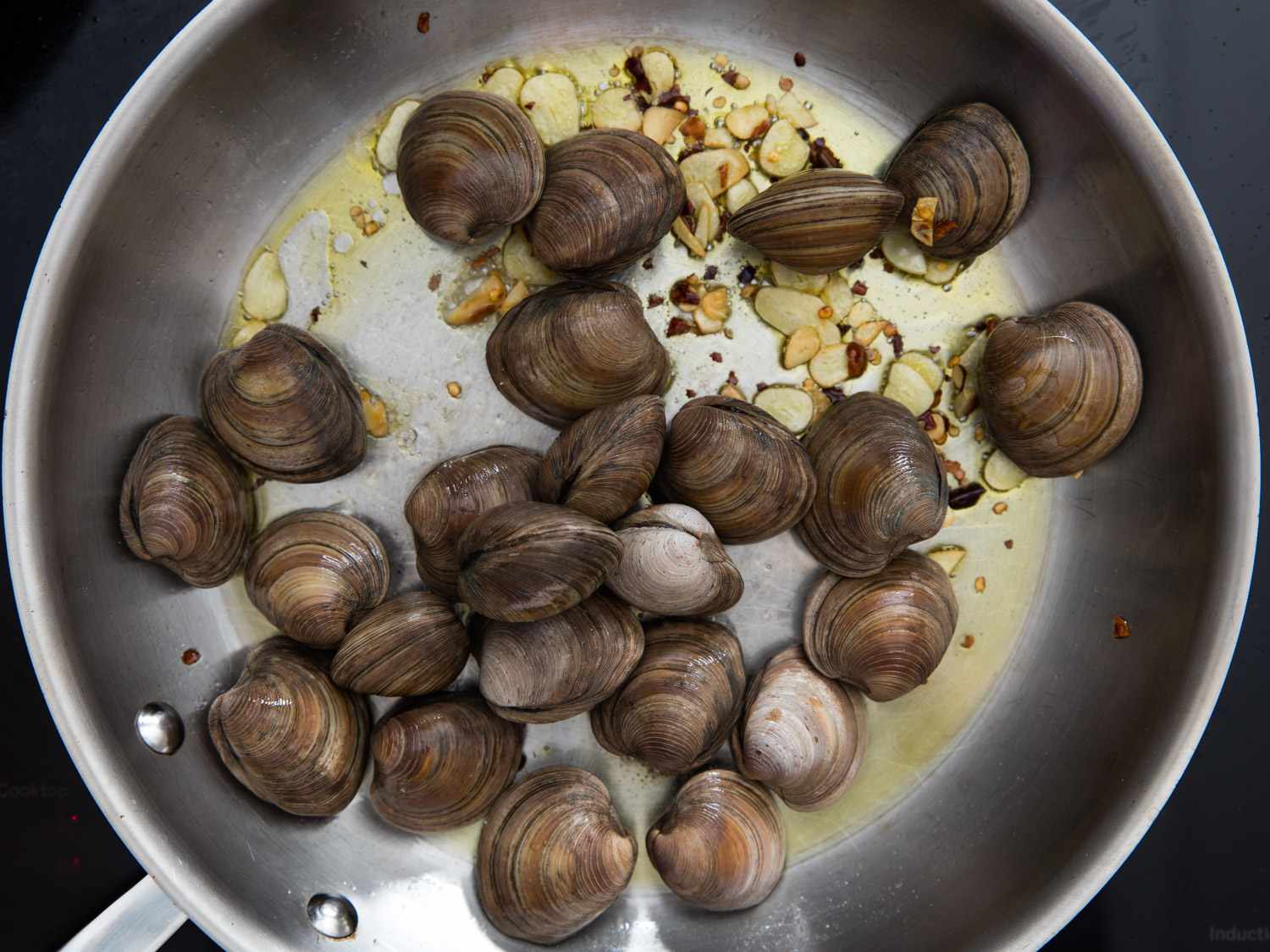 Clams resting in a skillet with garlic, olive oil, and red pepper flakes