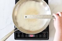 A person measuring a toasted flour hot spot in a pan on an induction burner