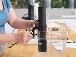 A person attaches a sous vide machine to a plastic Cambro container