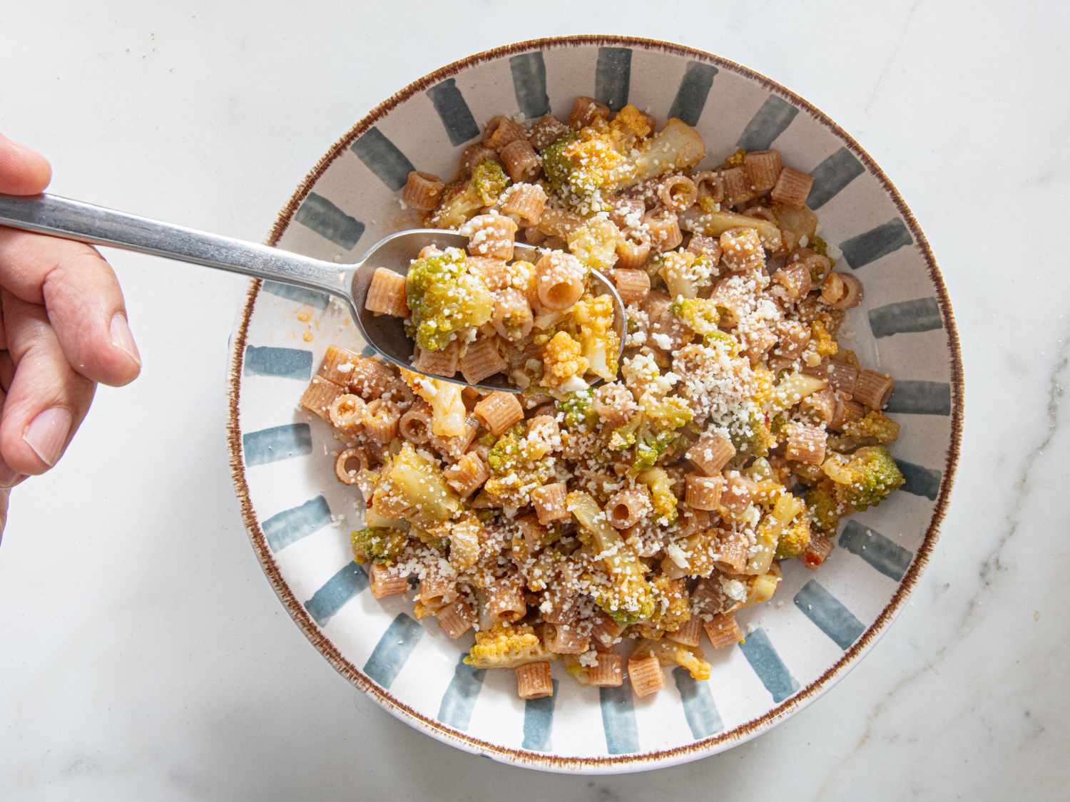 Bowl of pasta with broccoli and breadcrumbs hand holding a spoon