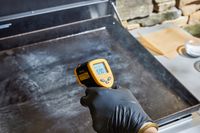 A person measures the temperature on the top of the Weber 36 Inch Gas Griddle