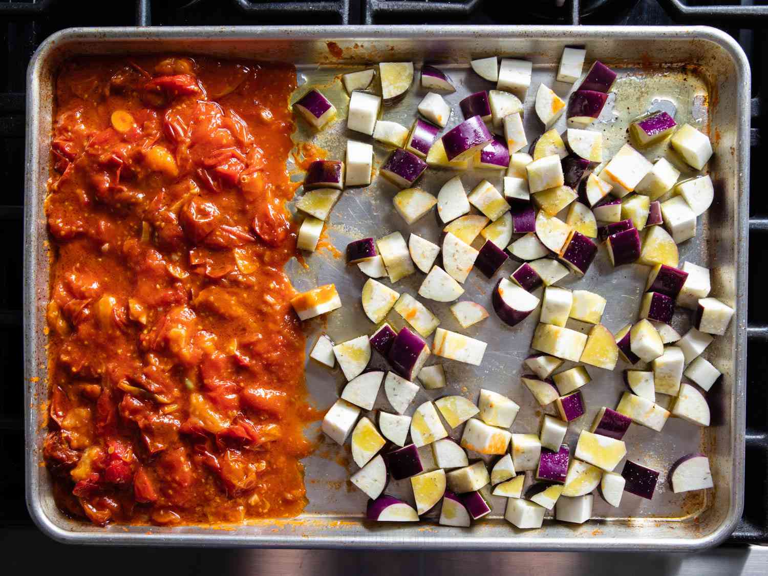 Mashed roasted tomatoes next to cubes of raw eggplant on a sheet pan