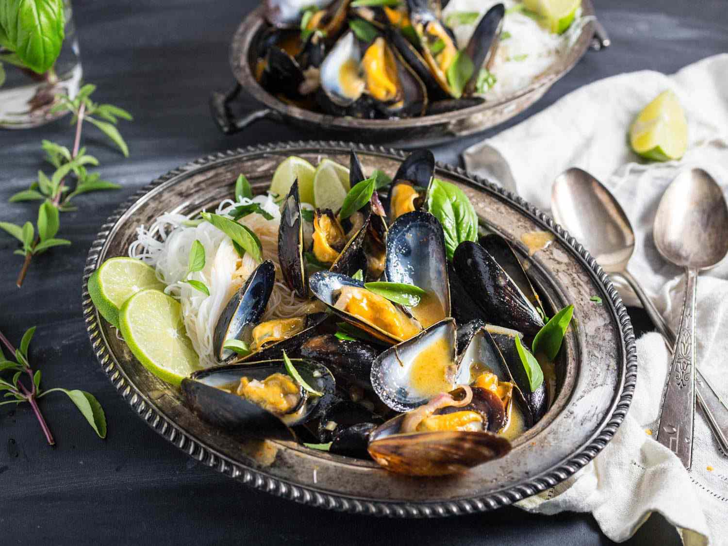 Mussels with Thai red curry broth on a metal platter with rice noodles.