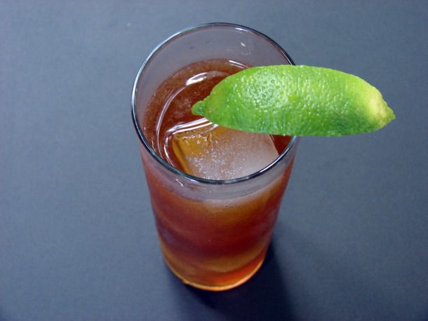 Cuba Libre cocktail in a Collins glass on grey background.