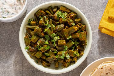 A bowl of spiced okra garnished with cilantro served on a table with side dishes