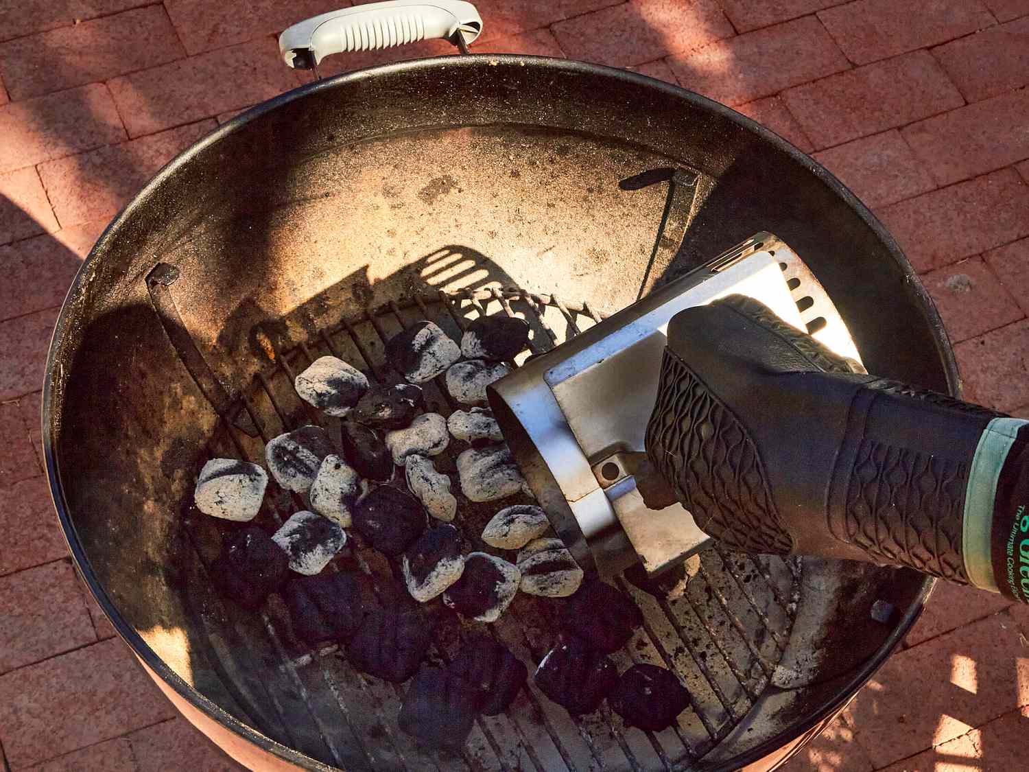 A hand with a heatresistant glove adjusts charcoal inside a grill using a chimney starter preparing for grilling