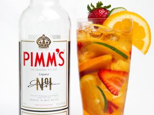 A bottle of Pimm's liqueur next to a fully garnished tall glass of Pimm's Cup cocktail.
