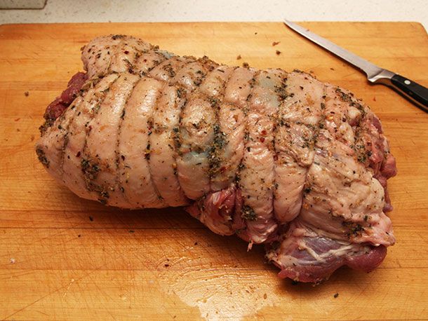 A rolled and tied boneless raw lamb leg roast resting on a cutting board.