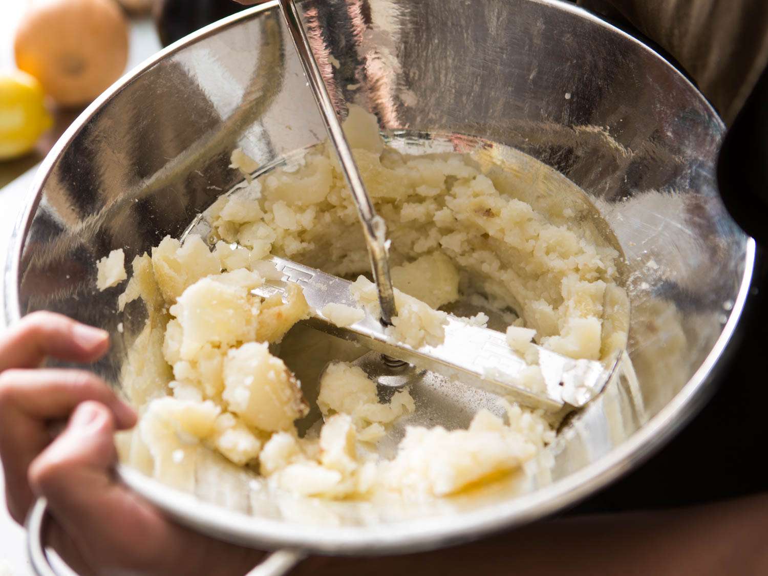 Cooked potatoes being processed in a stainless steel food mill.