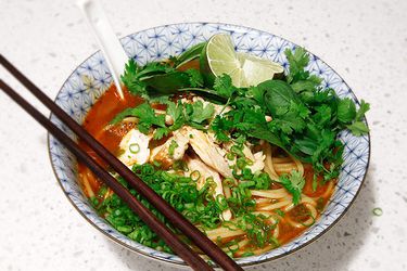  A bowl of Thai Red Curry Noodle Soup With Chicken, with soup spoon and chopsticks.