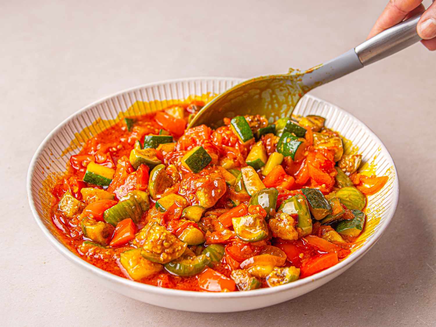 A bowl of Nigerian egg sauce being stirred with a spoon colorful ingredients include vegetables like tomatoes and peppers