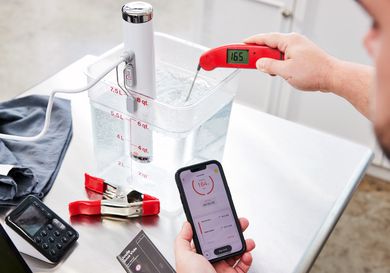 Person testing temperature of water in a bucket with the Breville Joule Sous Vide