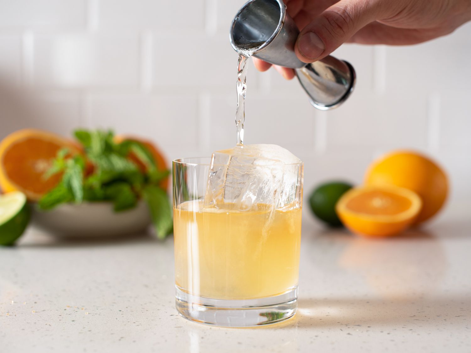 gin being poured from a jigger into a rocks glass with ice