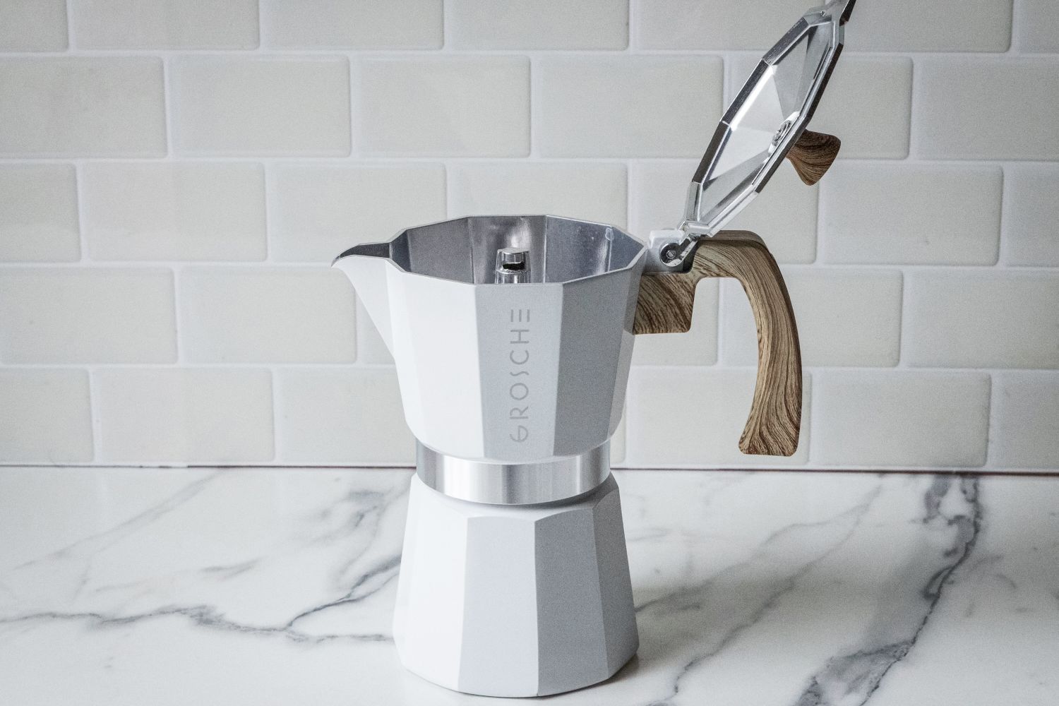 A stovetop espresso maker with an open lid and wooden handle on a marble surface
