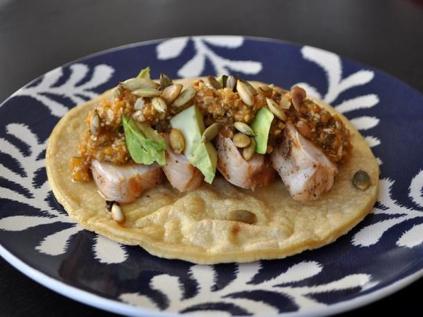 Sliced grilled chicken and sliced avocado arranged on corn tortillas, topped with pumpkin seed sauce and toasted pumpkin seeds