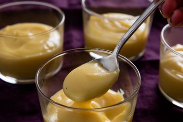 Four servings of butterscotch pudding. A spoonful of butterscotch pudding is held up to the camera.