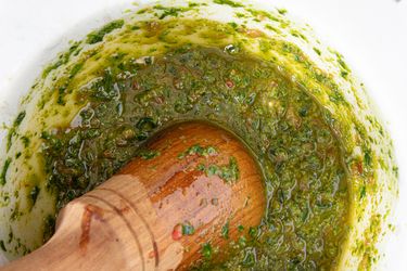 A mortar and pestle filled with a green herb-based sauce (pistou)