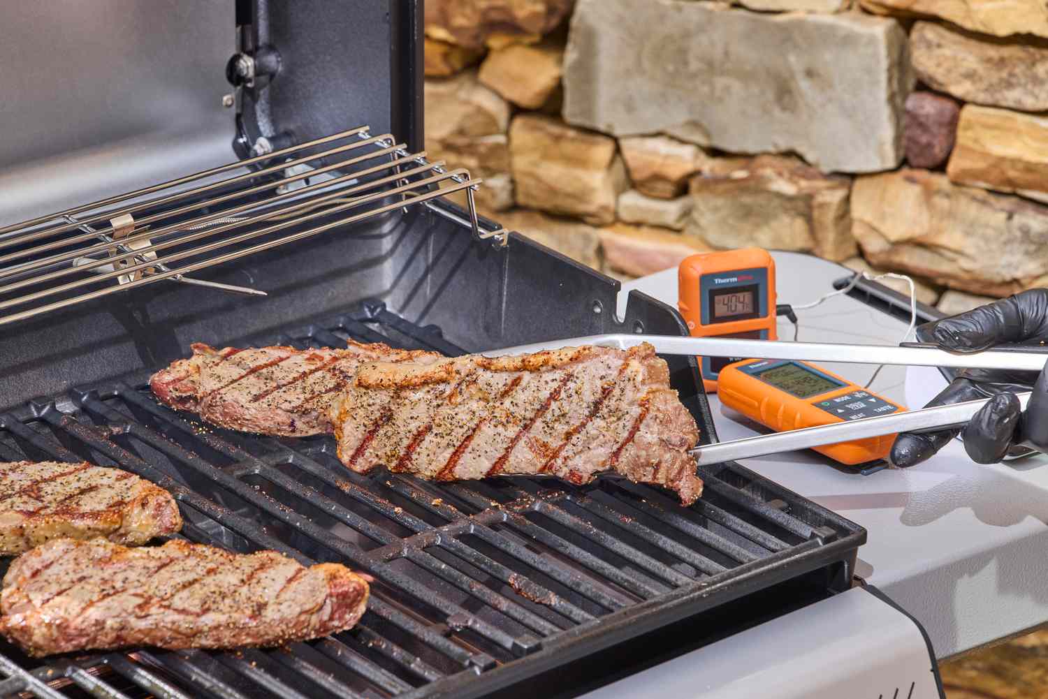 A gloved hands using tongs to lift a steak off of the Weber Spirit E-310 Gas Grill