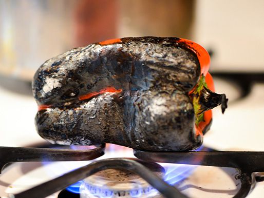 Closeup of a red bell pepper being charred over a gas heating element.