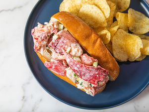 Overhead view of a stuffed lobster roll on a blue plate with potato chips