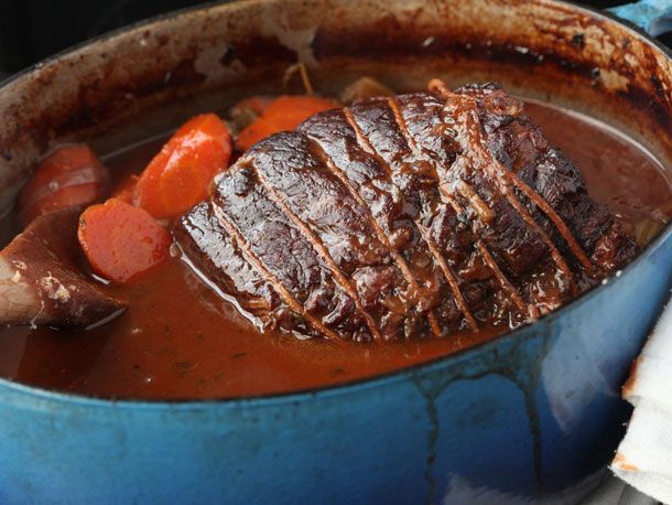 An oval dutch oven containing chunks of carrots and a braised piece of meat wrapped in twine.