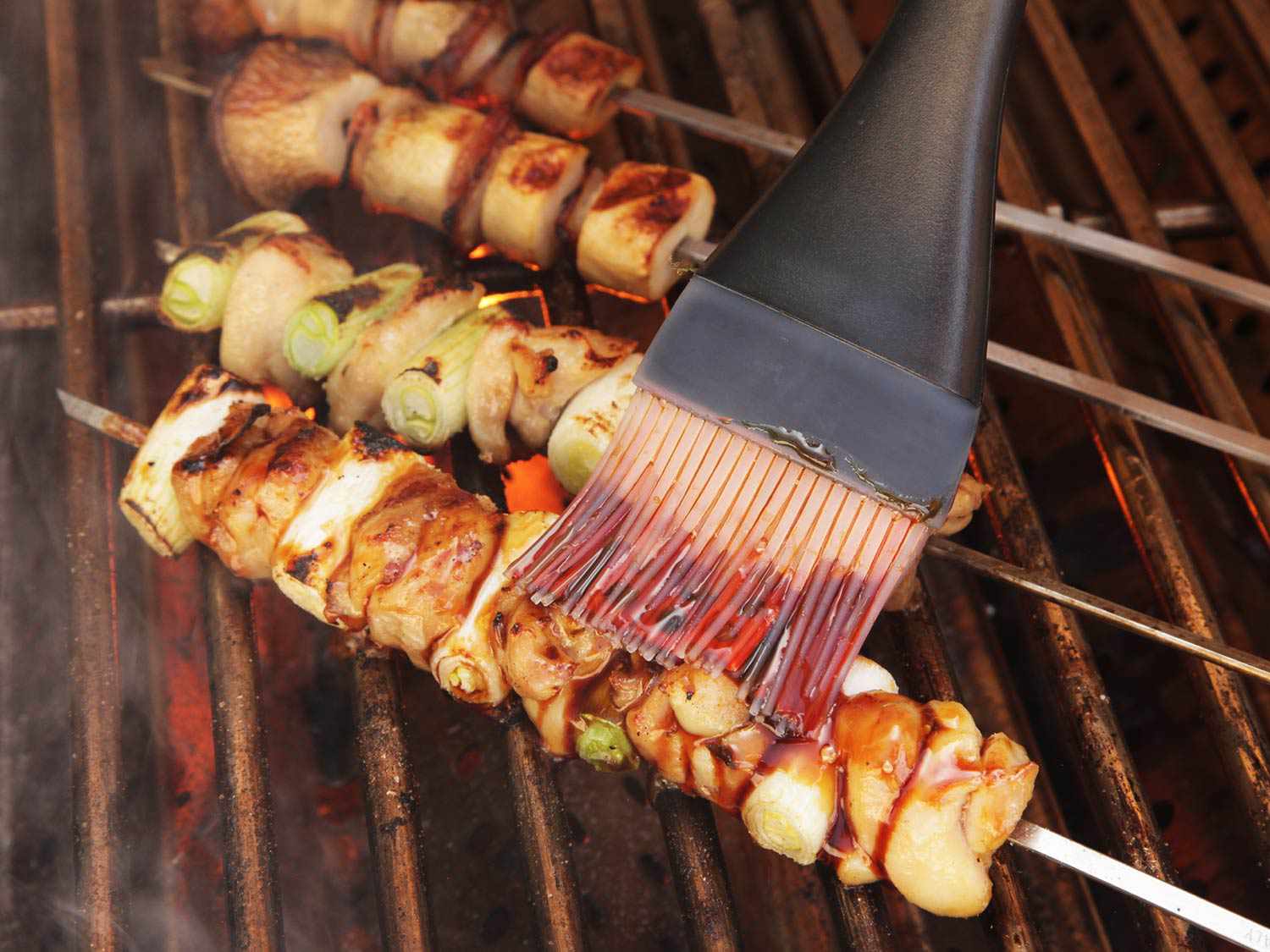 Brushing glaze onto negima yakitori skewers with scallions. 