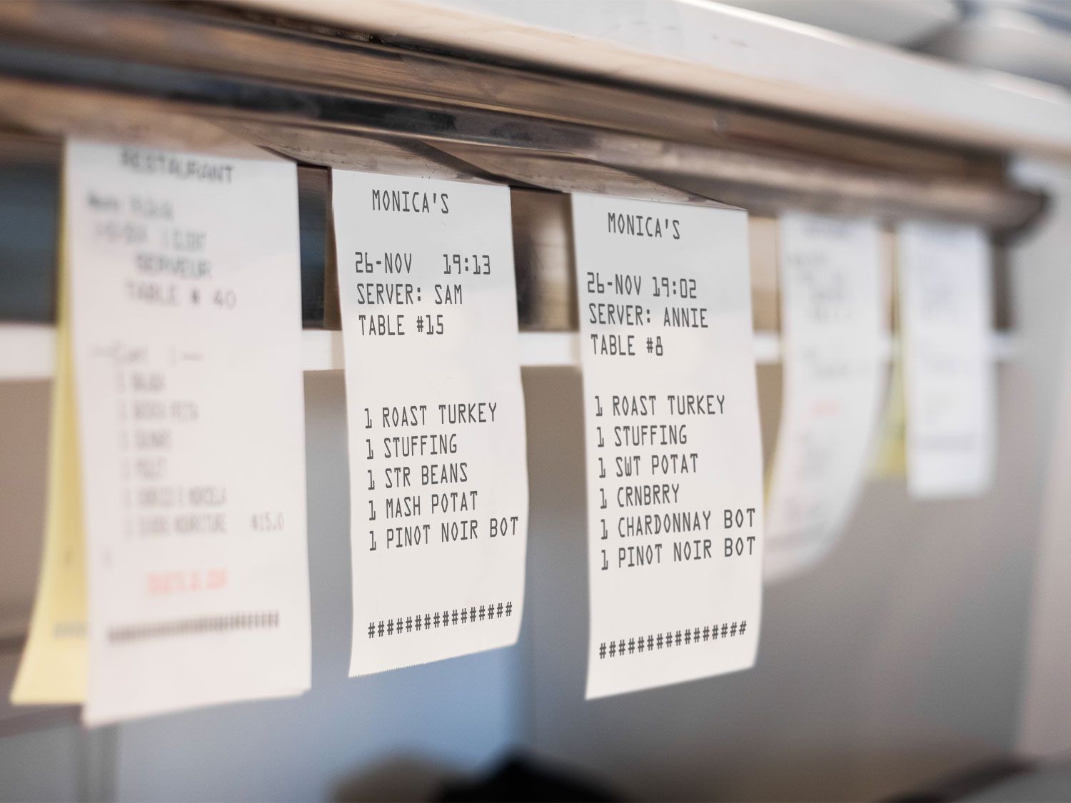Multiple restaurant tickets hanging from a metal bar.