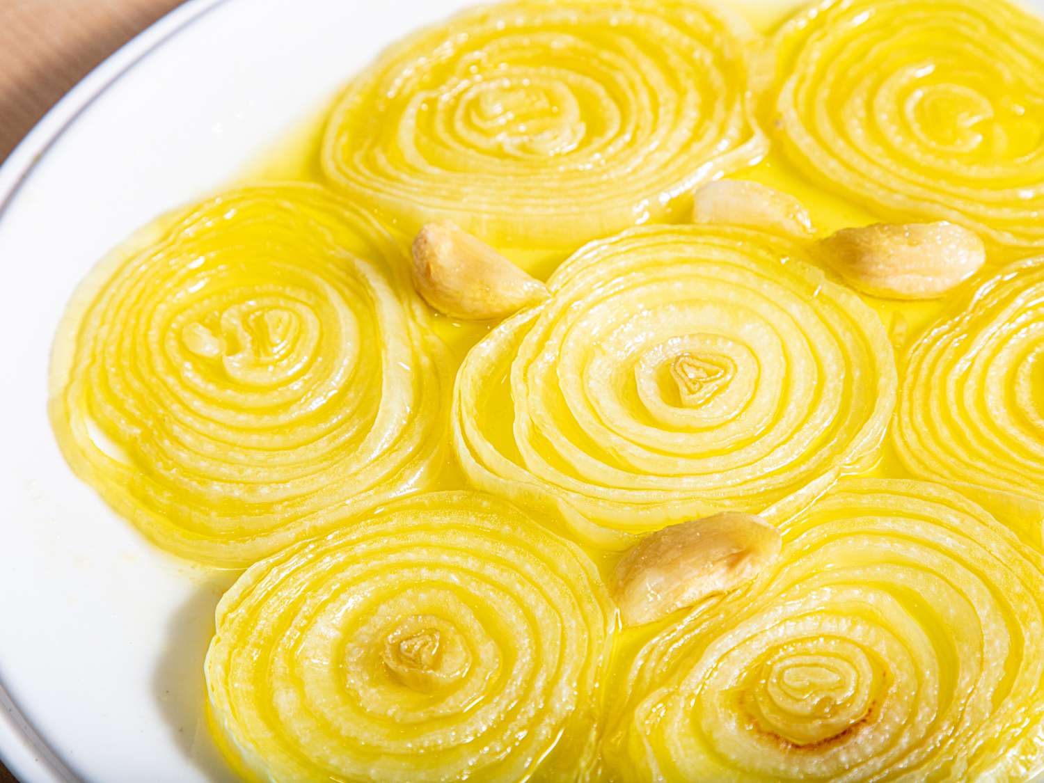 Circular slices of cooked onions and cloves of garlic on a white plate