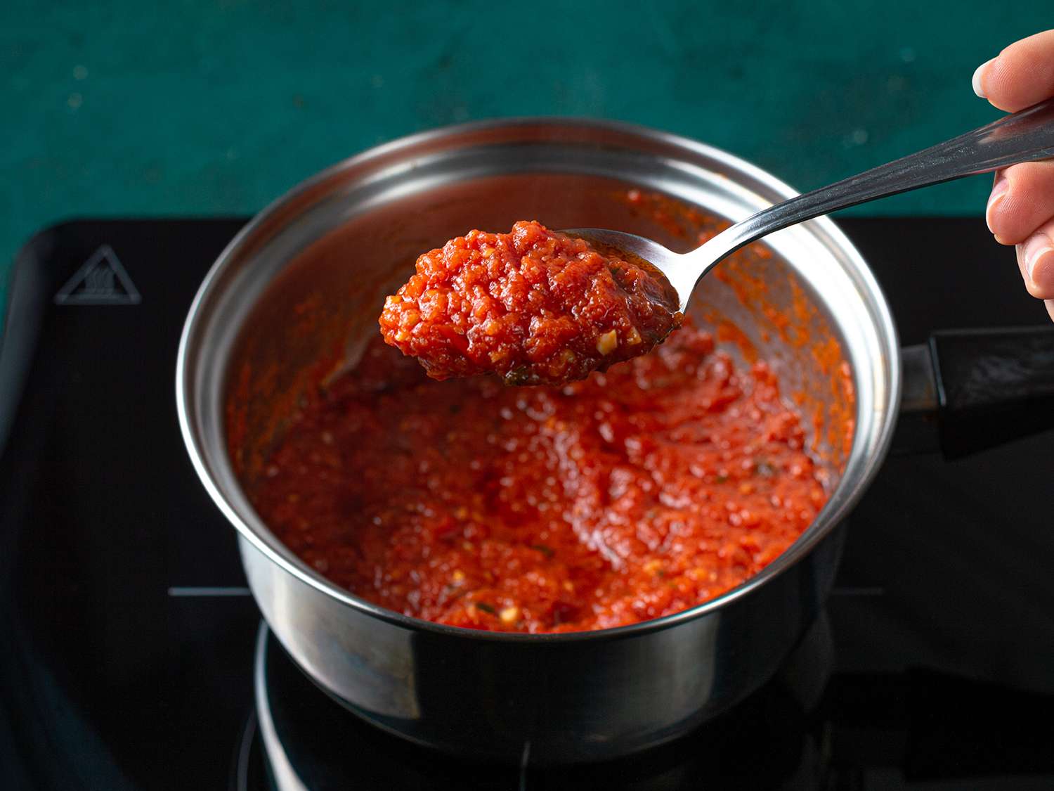Reduced tomato sauce being lifted out of the pot with a spoon.