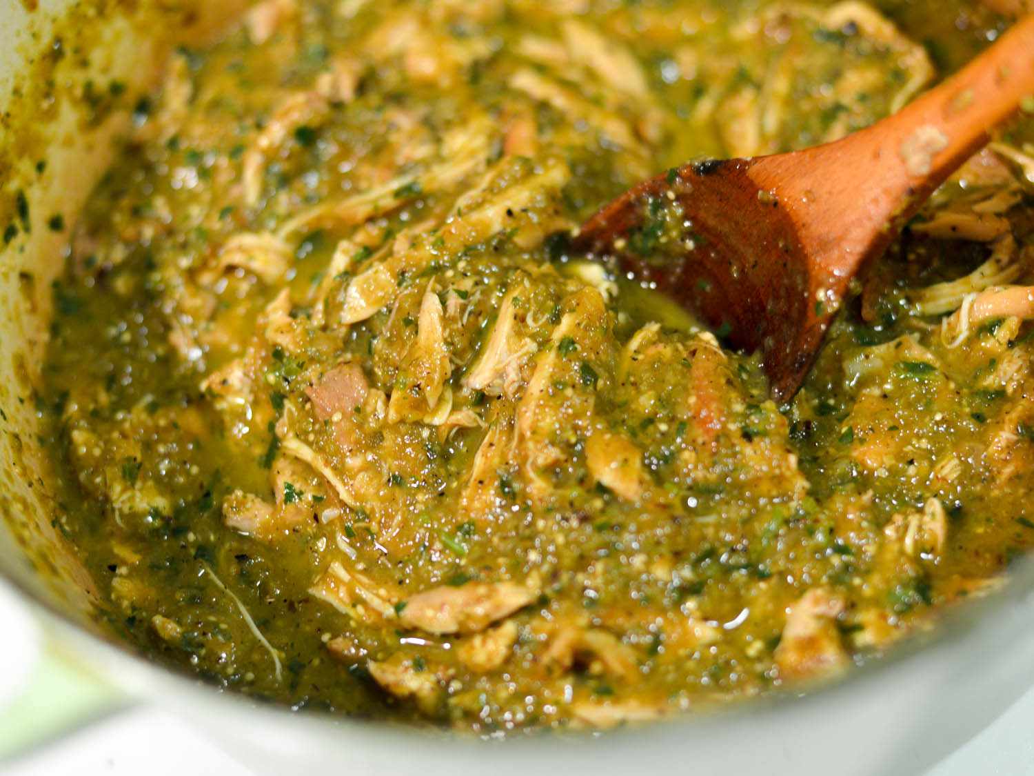 Stirring shredded chicken in roasted green chile sauce with wooden spoon