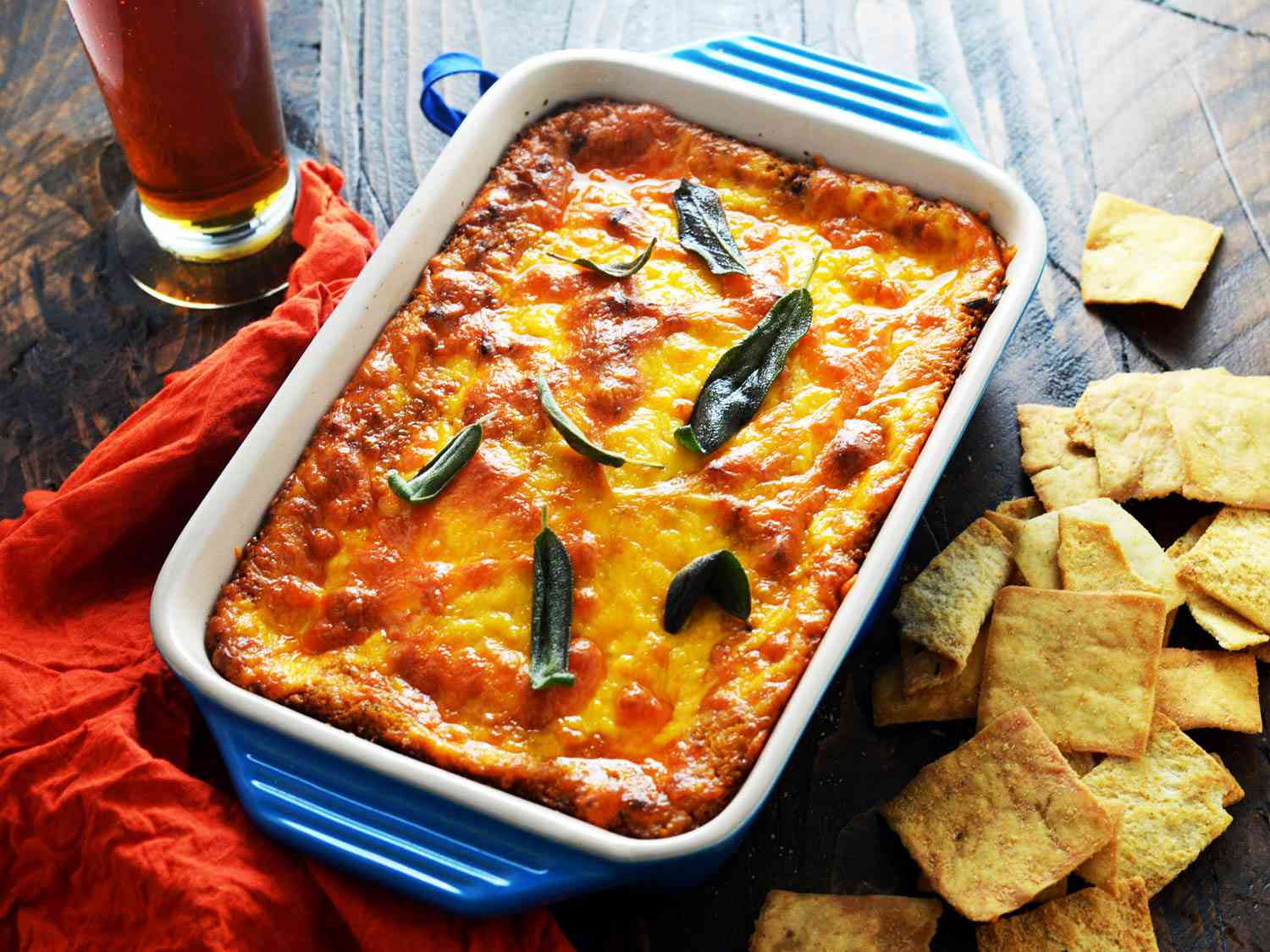 Butternut squash and cheddar dip in a baking dish, garnished with frazzled sage leaves, served with pita chips. 