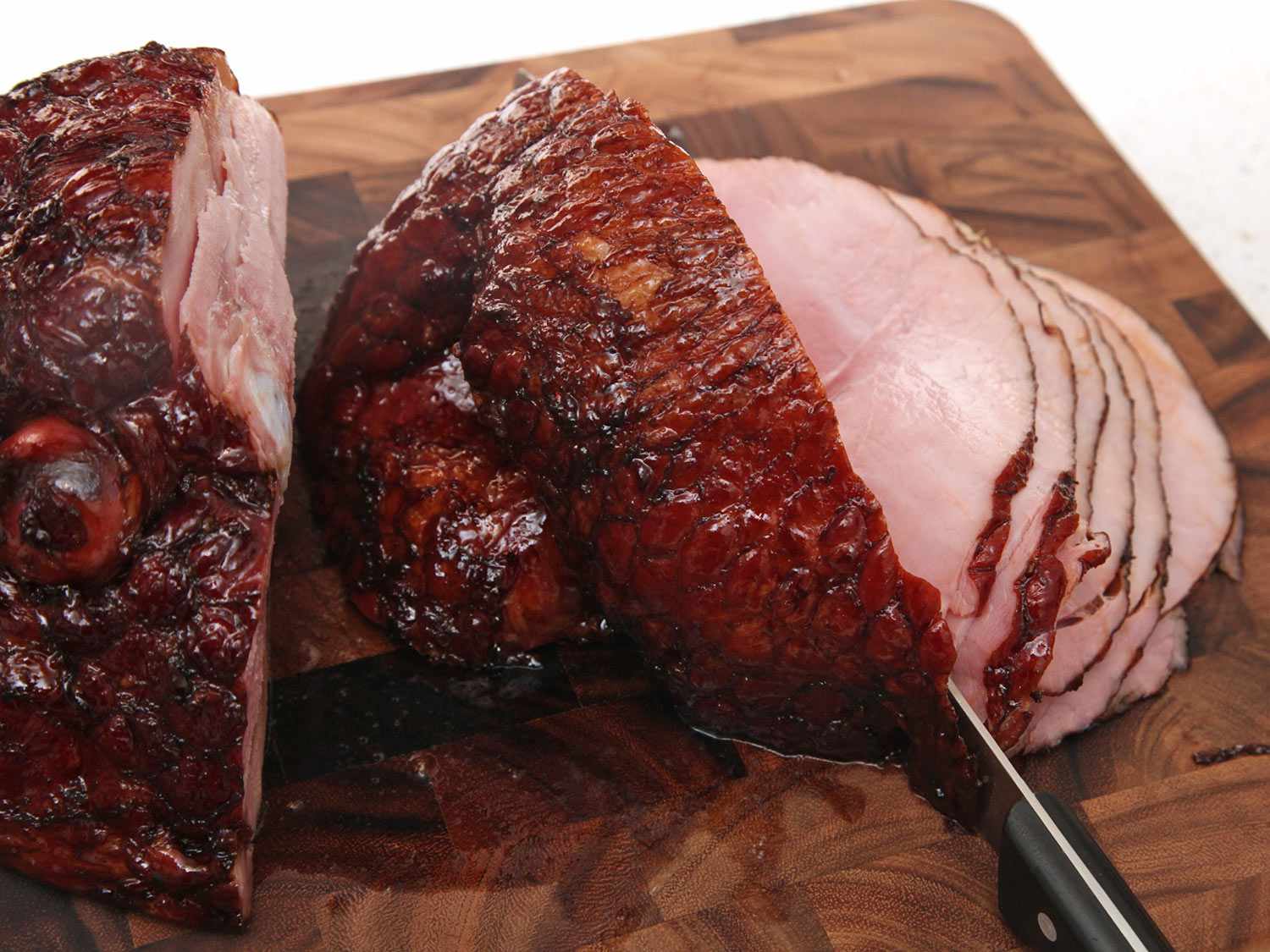 A carving knife slicing into glazed ham on a cutting board. 