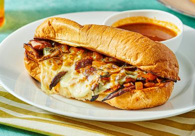 Vegetarian French dip sandwich with cheese and grilled vegetables on a platter, served with a cup of dipping broth