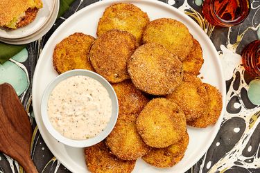 Overhead of Fried Green Tomatoes and dip on a printed surface. Plate on the corner has bitten tomatoes on it