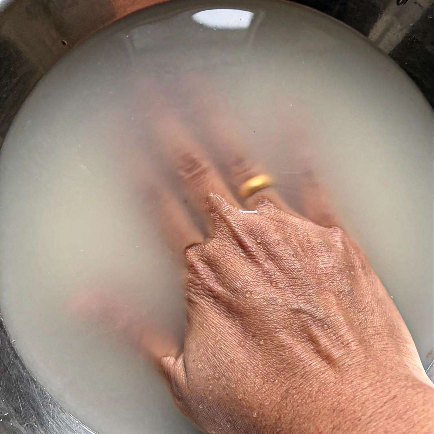 A hand submerged in water washing rice in a bowl