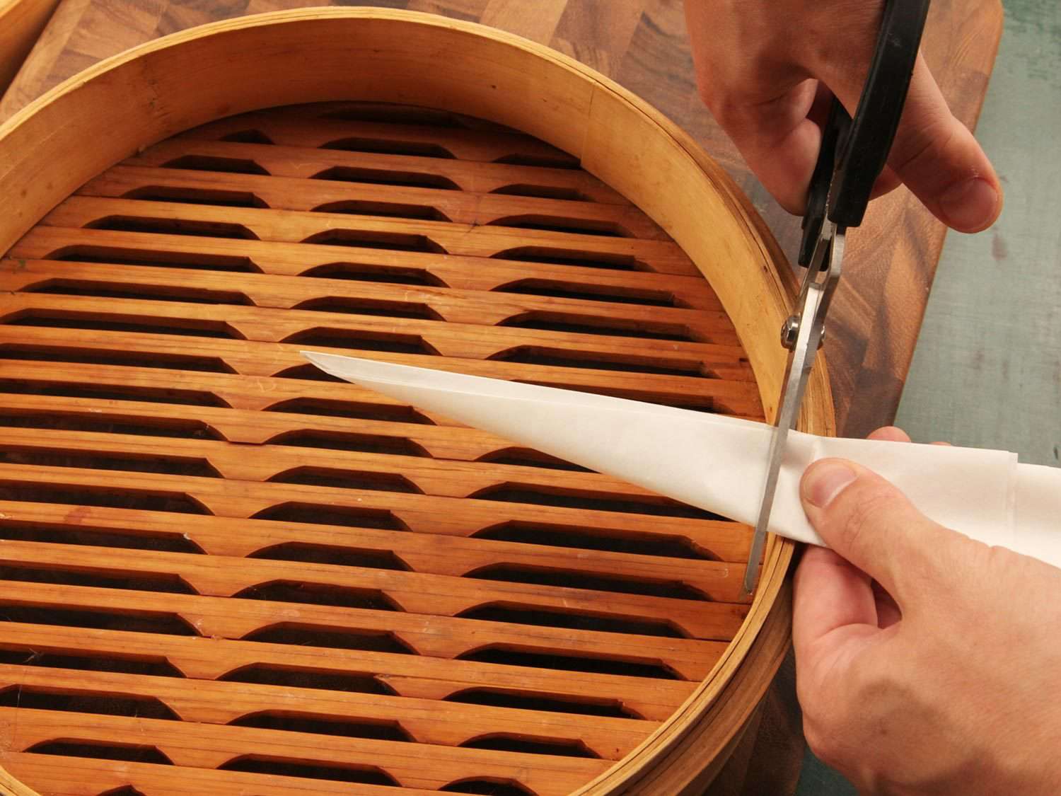 Cutting parchment paper to fit in a steamer basket.